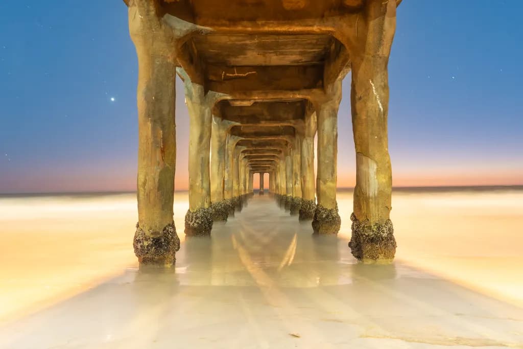 Serenity Beneath the Pier: A Sunset Reflection Over the Ocean's Embrace