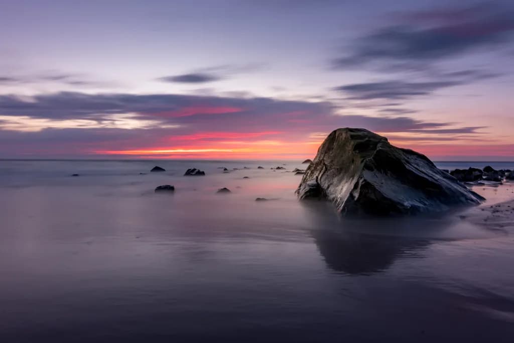 Serene Sunset Over Tranquil Waters: A Beachscape with Rock Reflections