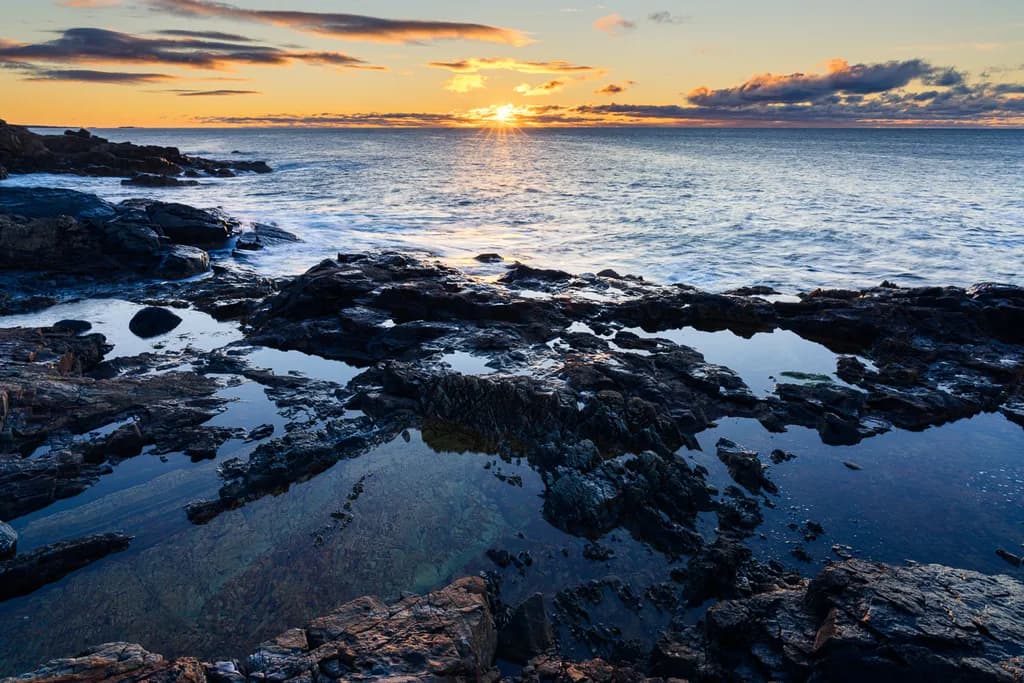 Tranquil Reflections: A Sunset Over Serene Waters and Rocky Shores