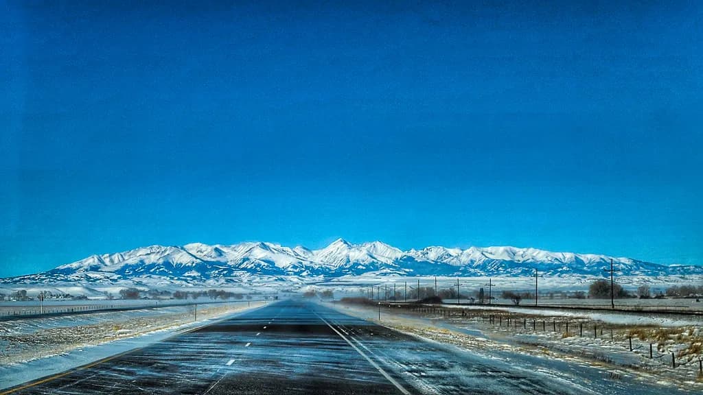 Majestic Journey: A Serene Winter Road Beneath the Snow-Capped Peaks