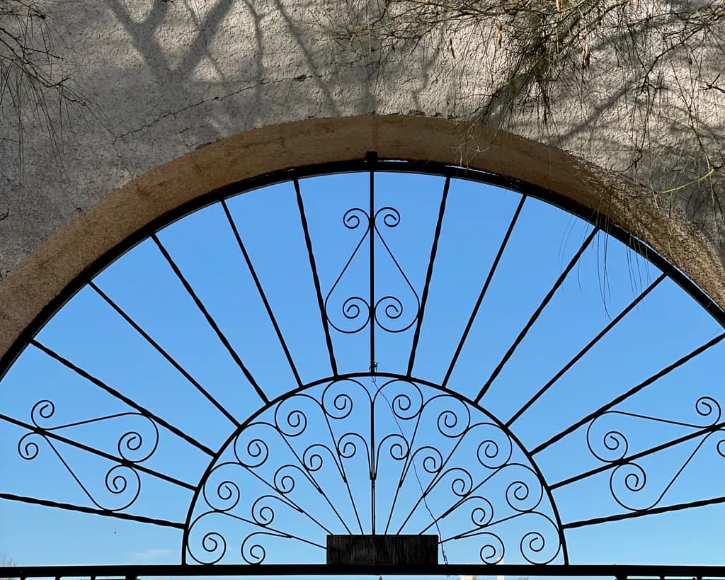 Whispers of Light: A Serene Iron Gate Framed by Sky and Shadow
