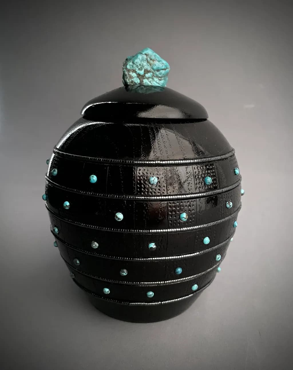 Ebon Elegance: A Striking Black Vessel Adorned with Turquoise Accents and a Unique Stone Lid