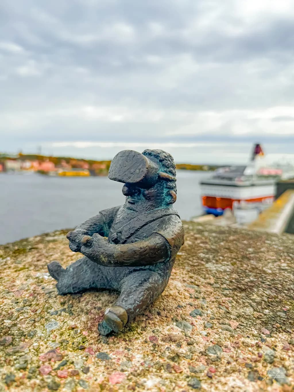 Whimsical Guardian of the Harbor: A Bronze Figure's Serene Watch Over the Waters
