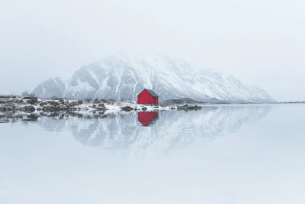 Whispers of Winter: A Solitary Red Cabin Reflected in a Snowy Landscape
