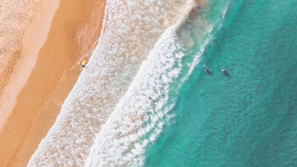 Serenity by the Shore: Aerial View of Waves and Sunlit Sands