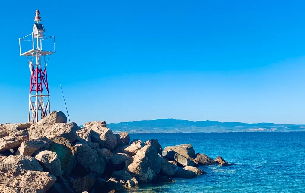 Serenity by the Sea: A Lighthouse's Embrace Amidst Rocky Shores and Endless Blue Skies