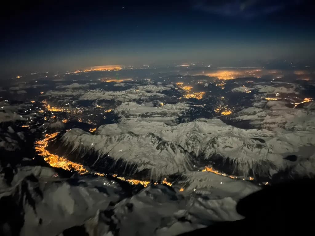 Whispers of Light: A Nighttime Aerial View of Snow-Capped Mountains and Glimmering Valleys