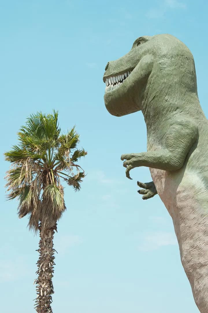 Majestic Giant: A T-Rex Among Palm Trees in a Clear Blue Sky