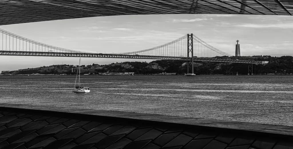 Whispers of the River: A Serene View of the Bridge and Sailboat in Black and White