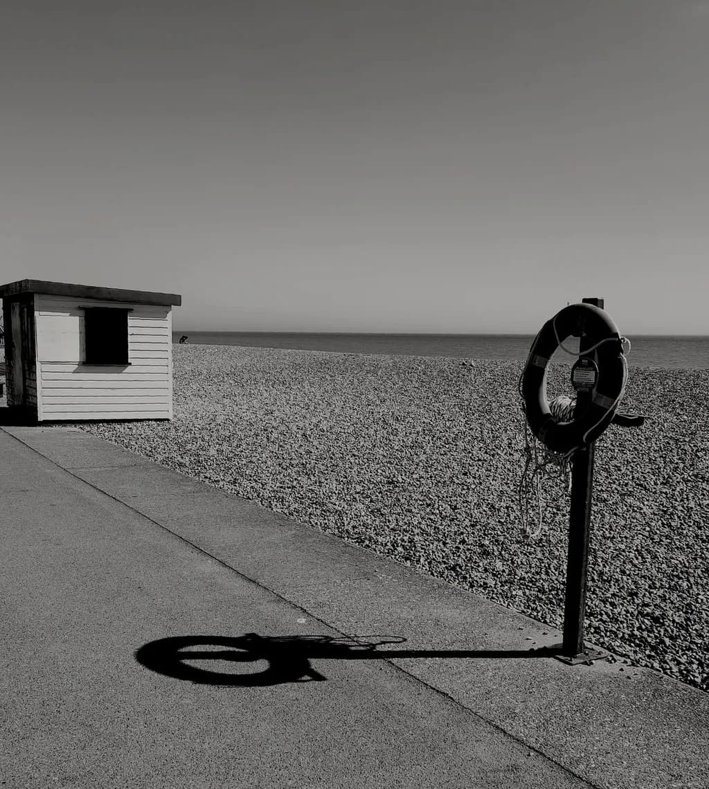 Monochrome Solitude: A Lifebuoy's Shadow on the Serene Coastline