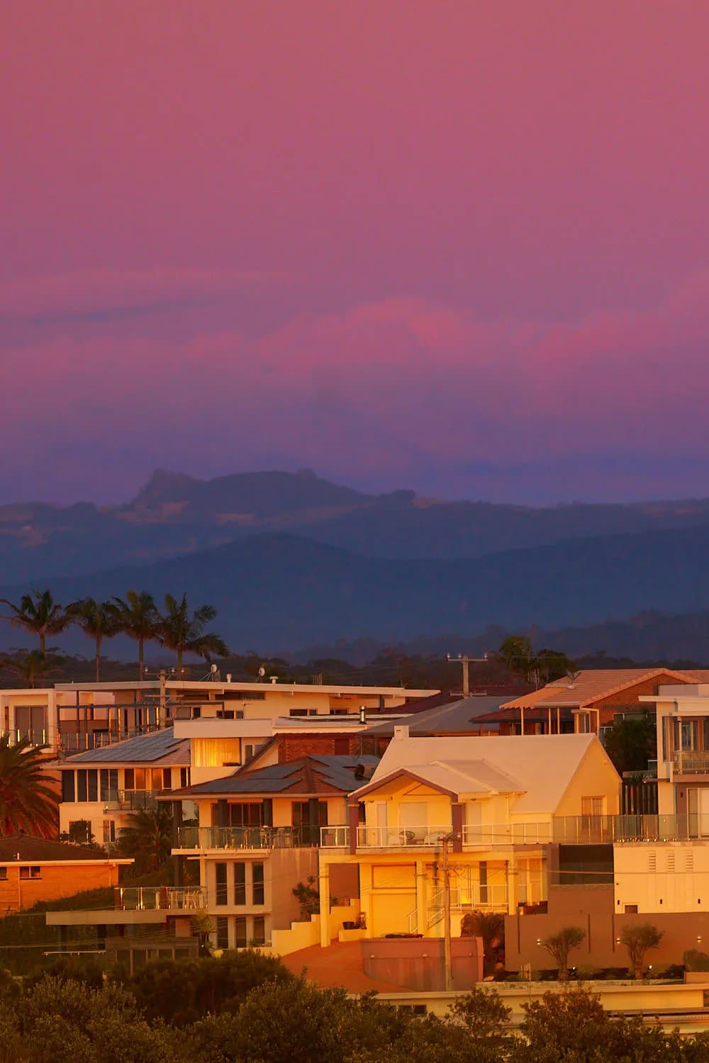 Serenity at Dusk: A Vibrant Sunset Over Coastal Homes and Majestic Mountains