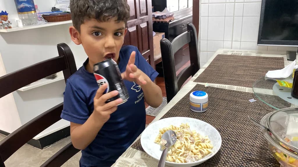 Joyful Moments: A Playful Child Enjoying Pasta and a Refreshing Drink at Home