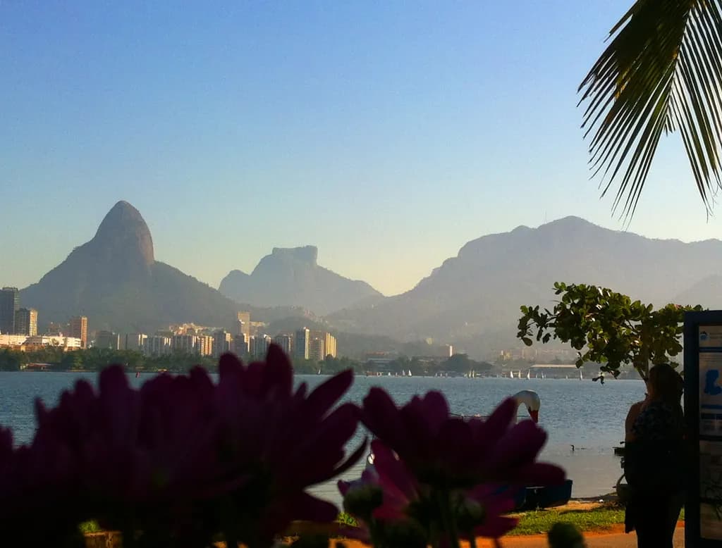 Serenity at Dusk: A Vibrant Sunset Over Mountains and Cityscape with Blossoming Flowers in the Foreground