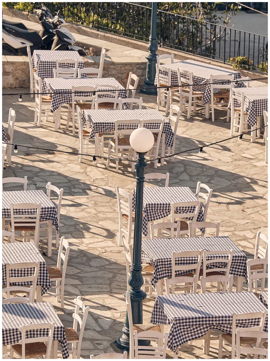 Charming Mediterranean Café: A Serene Outdoor Dining Scene with Checkered Tables and Soft Sunlight