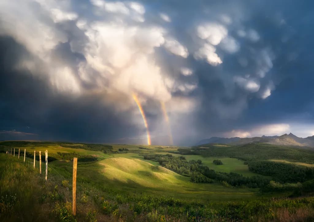 Whispers of Light: A Dual Rainbow Emerges from Stormy Skies Over Verdant Hills