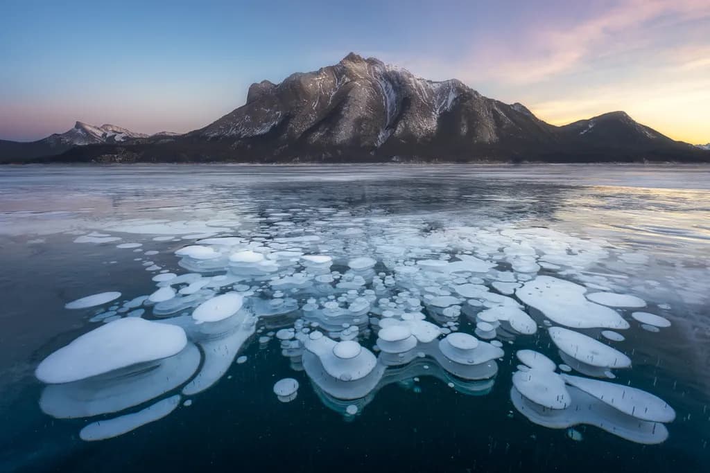 Frozen Serenity: A Winter Landscape of Ice Bubbles and Majestic Mountains at Dawn