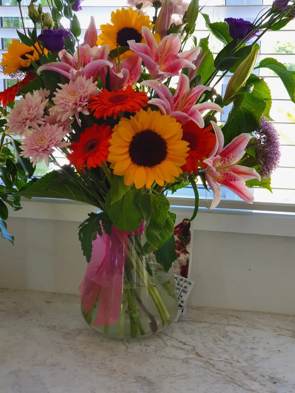 Vibrant Symphony: A Floral Celebration of Sunflowers, Lilies, and Gerbera Daisies in a Glass Vase