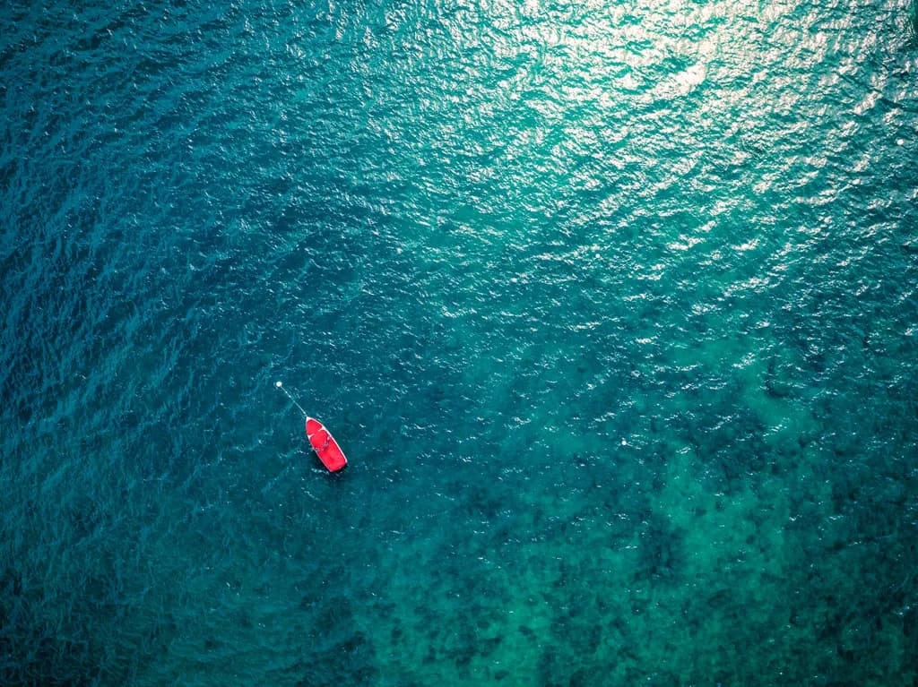 Serenity in Blue: A Drone's Eye View of a Red Boat on Tranquil Waters