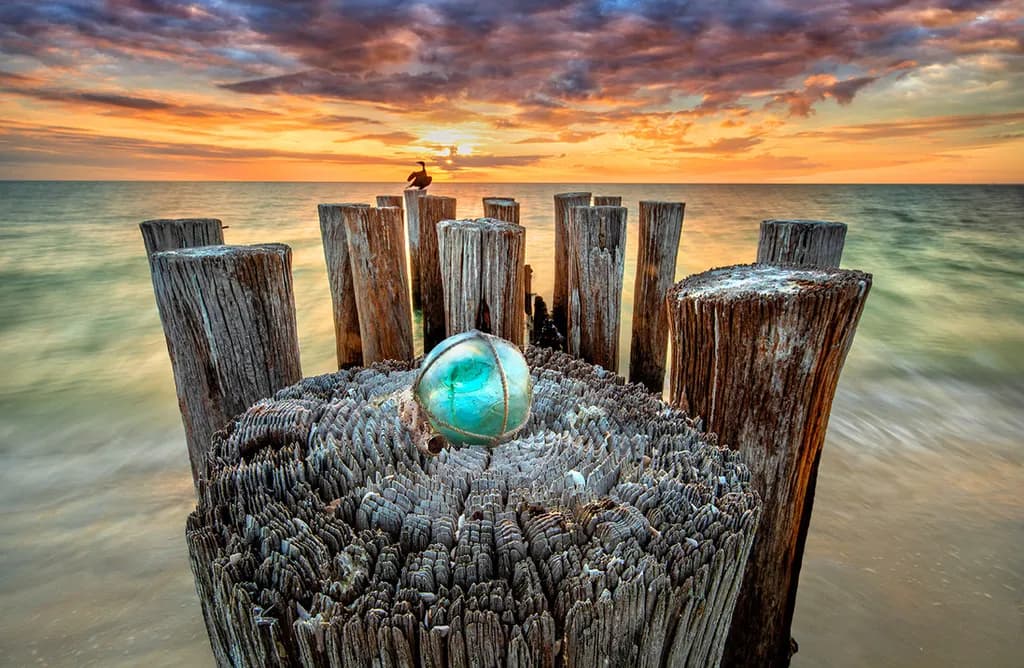 Whispers of the Sea: A Tranquil Sunset Over Weathered Pilings and a Glass Orb