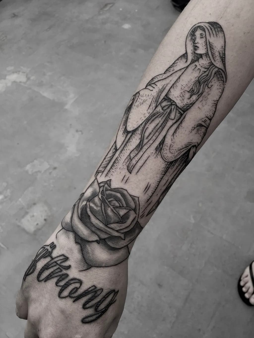 Ethereal Strength: A Black and Grey Tattoo of a Serene Figure and Rose