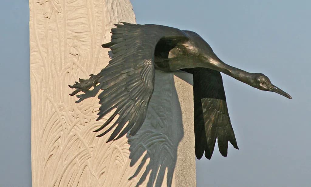 Ethereal Flight: A Bronze Crane in Motion Against Nature's Canvas