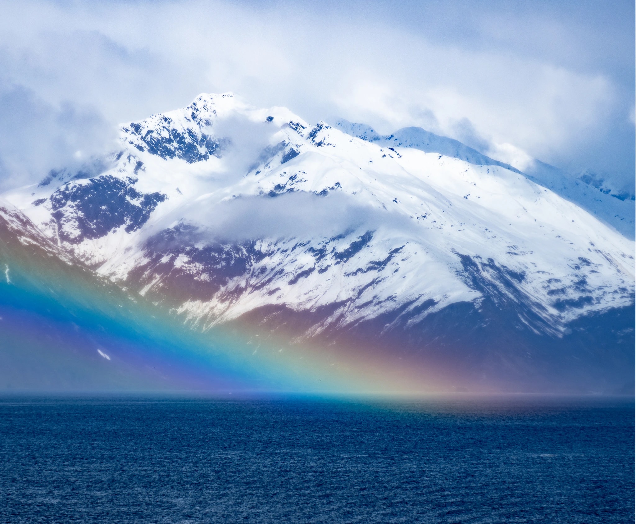 Majestic Harmony: A Rainbow's Embrace Over Snow-Capped Peaks and Serene Waters