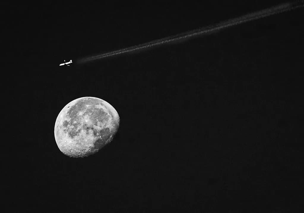 Celestial Journey: An Airplane's Dance with the Moon in Black and White Contrast