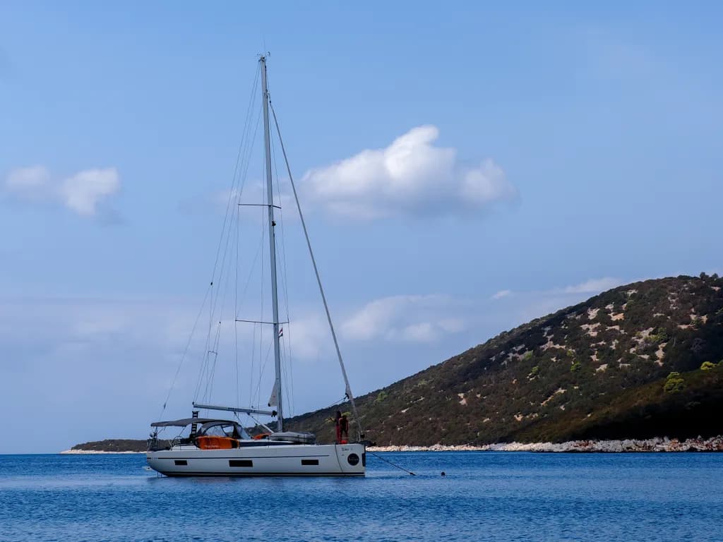 Serenity at Sea: A Sailboat Anchored in Tranquil Waters with Rolling Hills in the Background